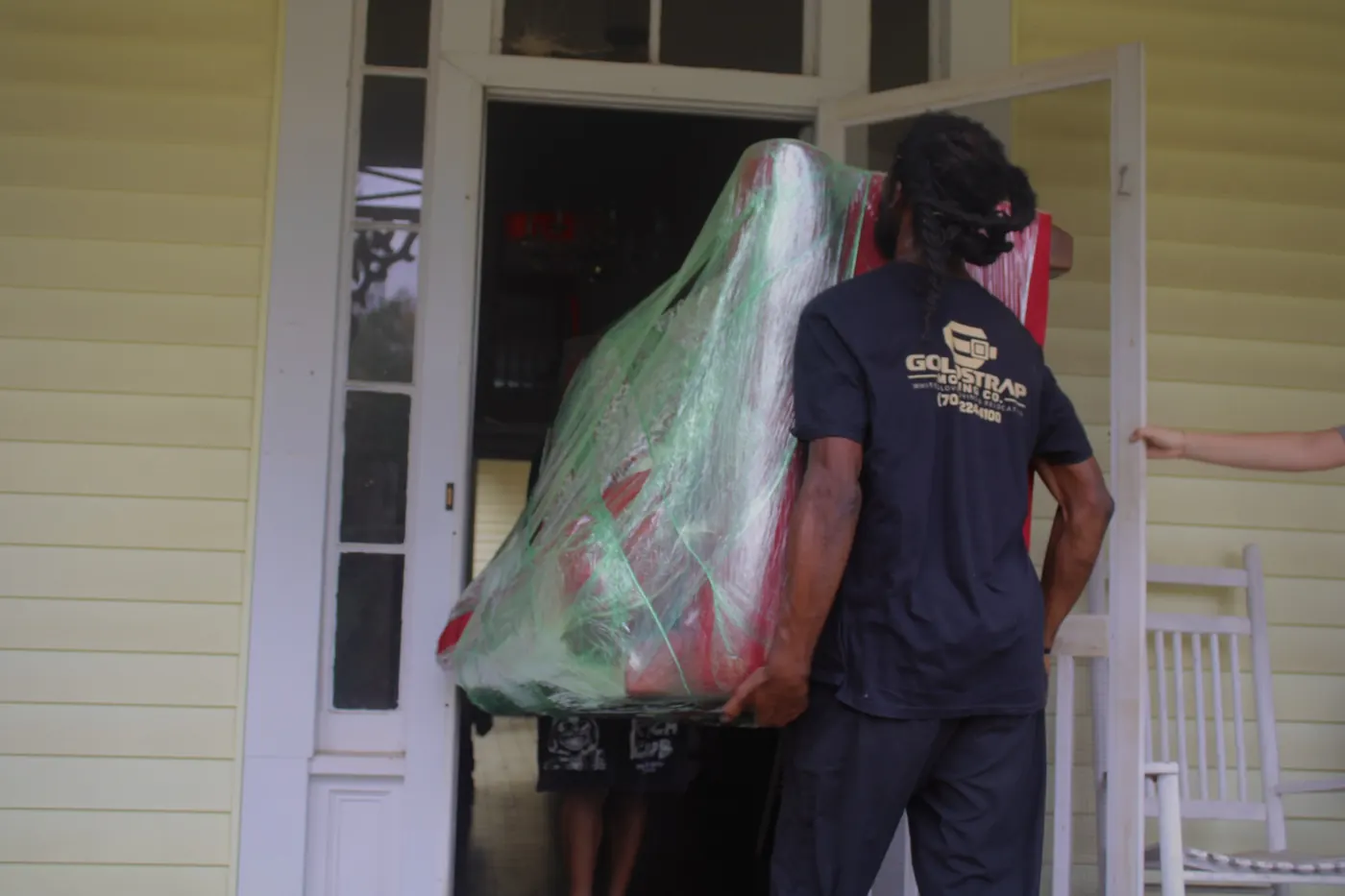 GoldStrap Moving crew carrying a wrapped sofa through the front door of a home in Union Point, GA