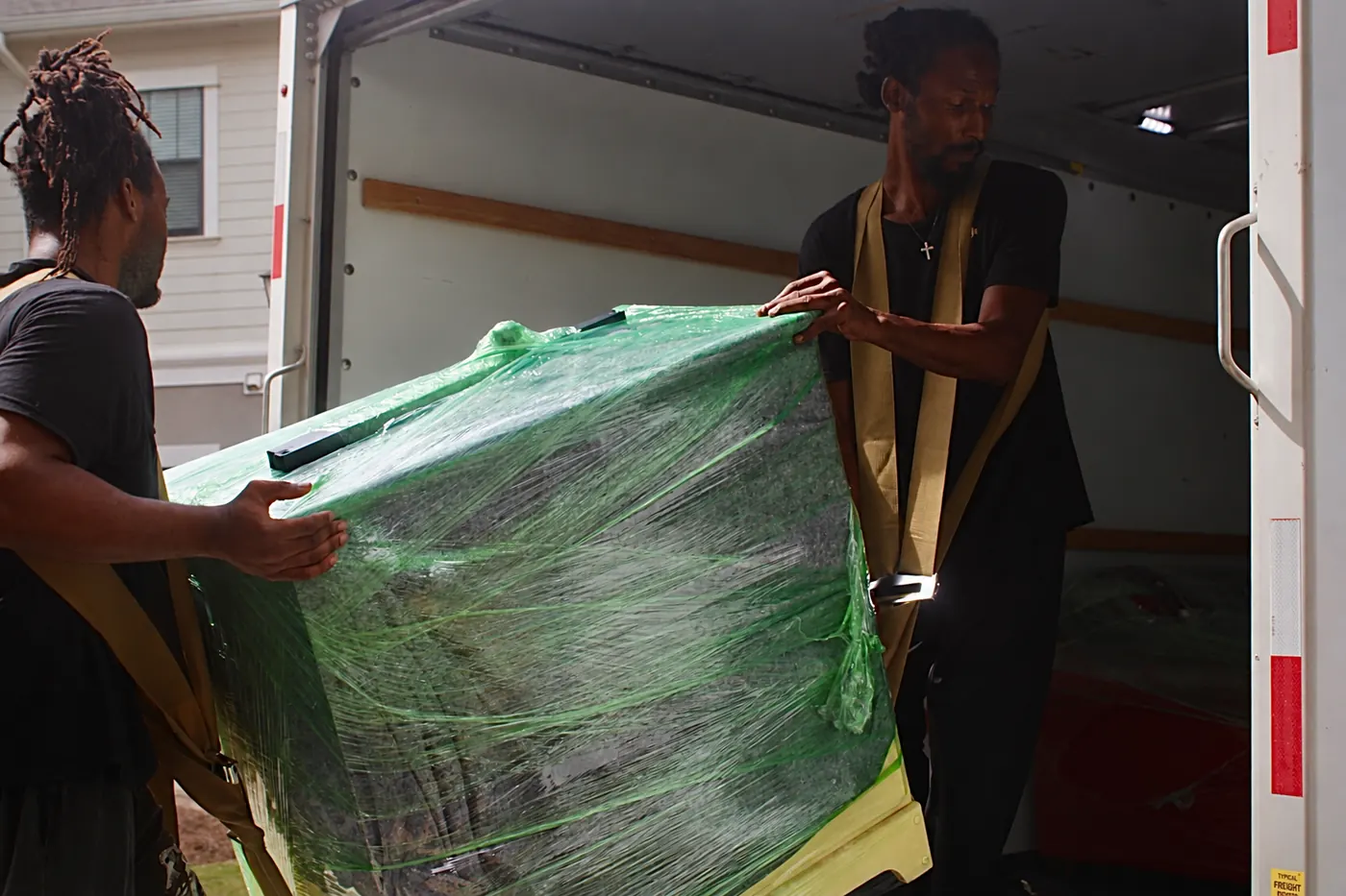 Two GoldStrap Moving crew members loading a padded and wrapped piece of furniture into the moving truck