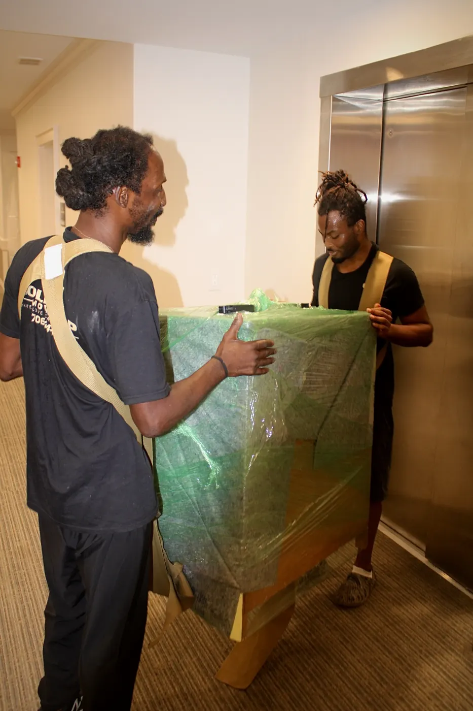 Two GoldStrap Moving crew members guiding a padded and wrapped piece of furniture into an elevator