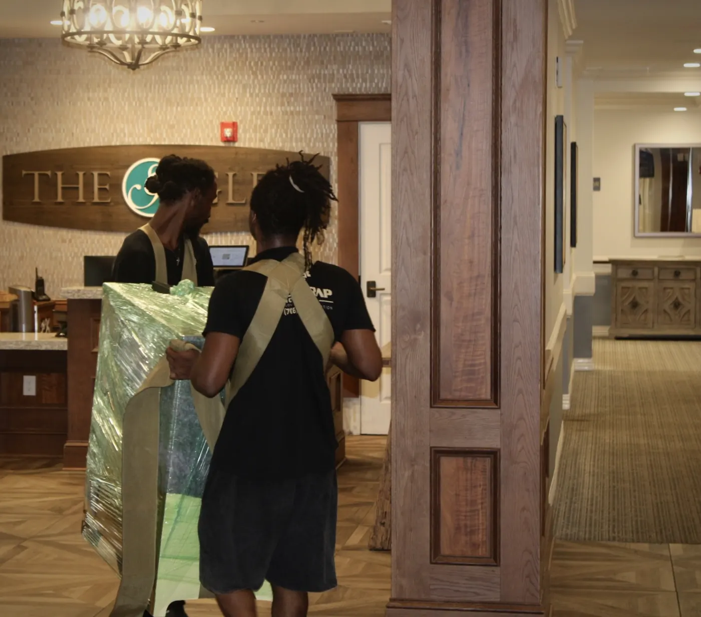 Two GoldStrap Moving crew members using shoulder straps to carry padded furniture through a lobby in Greensboro, GA