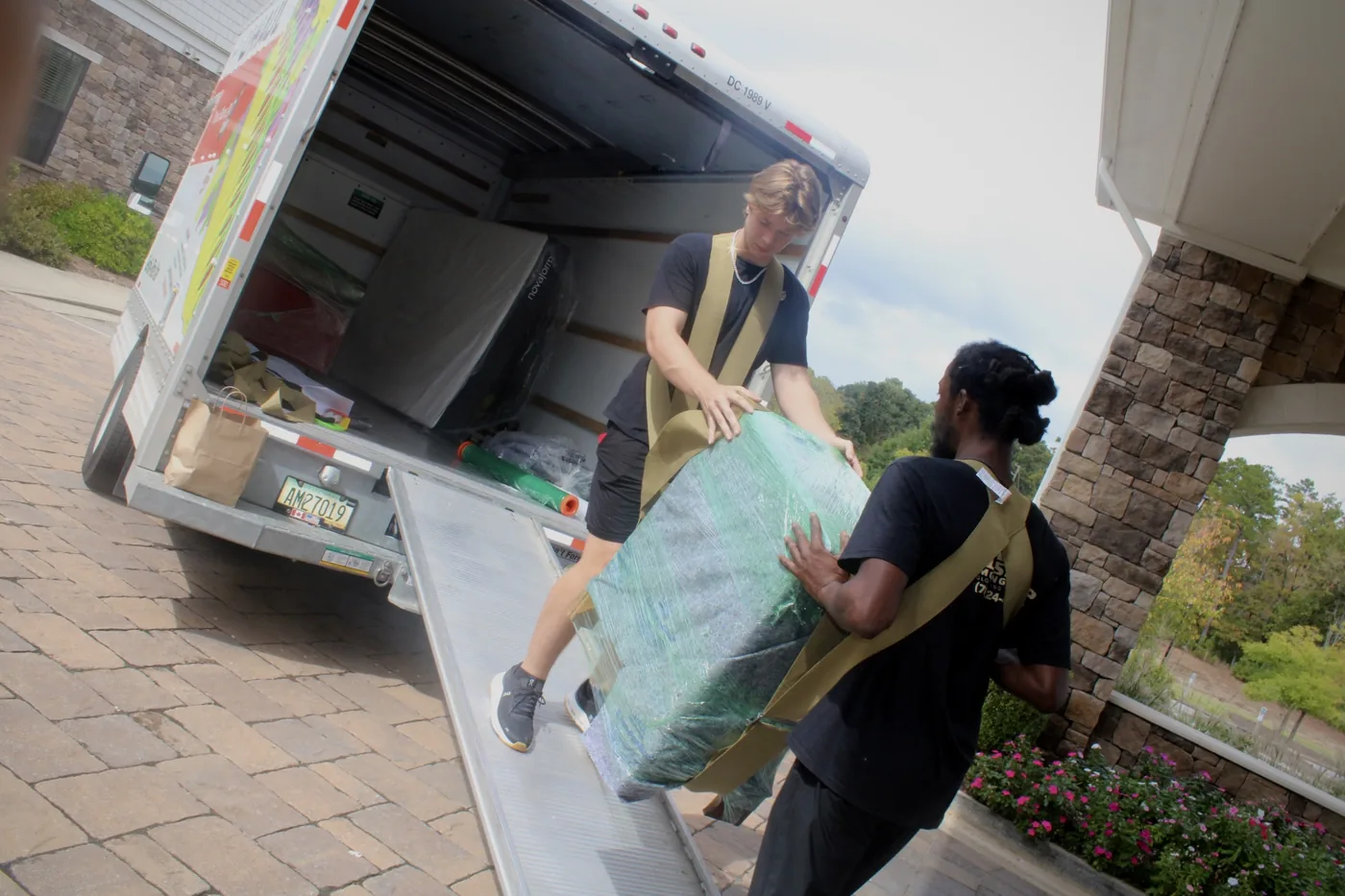 Two GoldStrap Moving crew members using shoulder straps to carry a padded, stretch-wrapped piece of furniture up the truck ramp near Lake Oconee