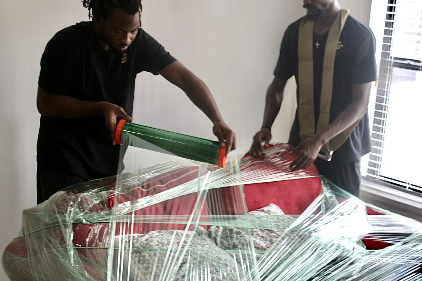 Two GoldStrap Moving crew members stretch-wrapping a red sofa before a move