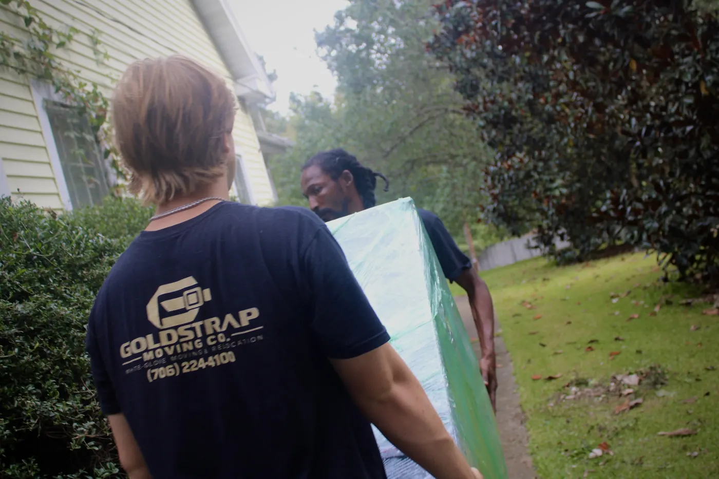 Two GoldStrap Moving crew members carrying wrapped furniture to a home in Union Point, GA