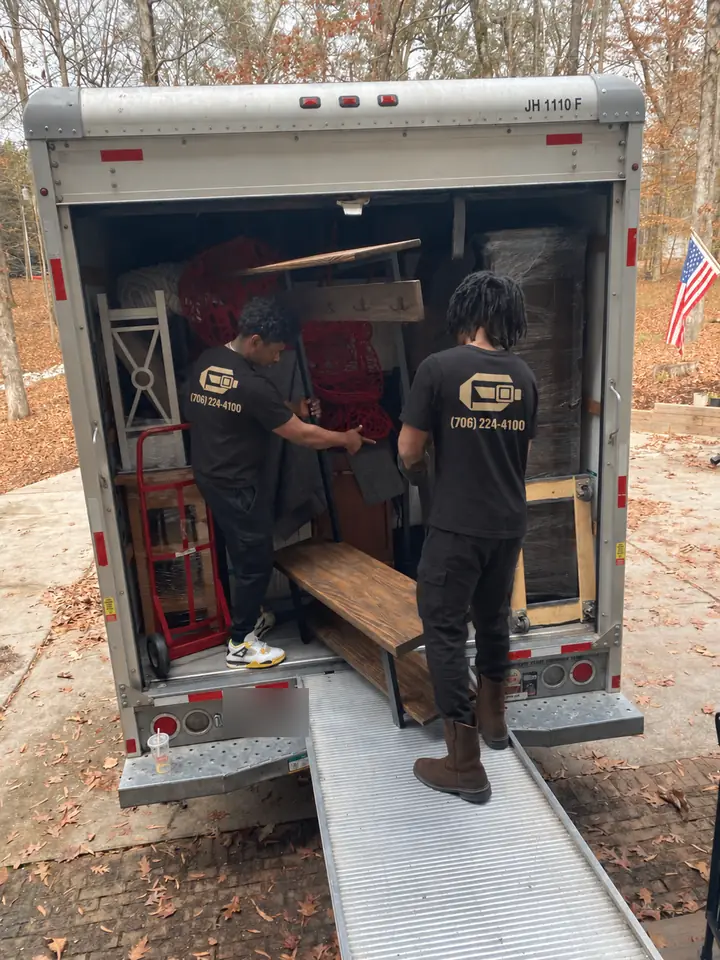 Two GoldStrap Moving crew members loading furniture into a moving truck using a ramp